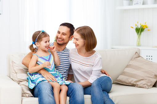 Happy family mother, father, and child daughter  laughing and hugging at home on sofa