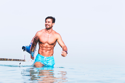 Cheerful fit man coming out of ocean with his surfing board.