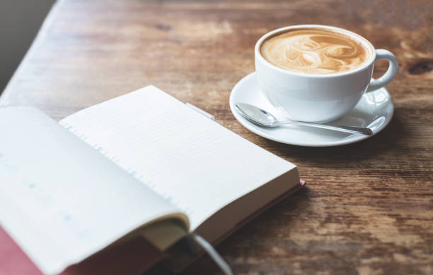 istock Open notebook with cup of coffee on wooden table. 670117612
