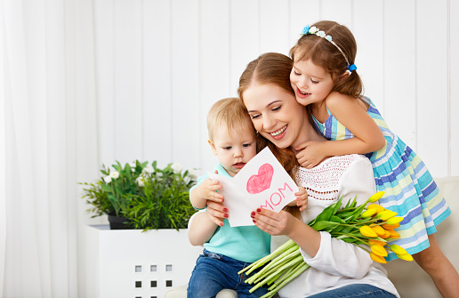 Happy mother's day! Children congratulates moms and gives her a postcard and flowers tulips