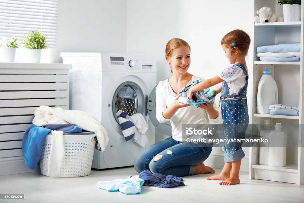 family mother and child girl  in laundry room near washing machine family mother and child girl little helper in laundry room near washing machine and dirty clothes Laundry Stock Photo