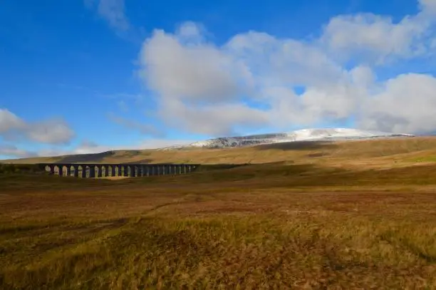 The snow covered peak in the distance is Whernside Hill, one of the Three Peaks of Yorkshire. The viaduct is the famous Ribblehead Viaduct on the Settle to Carlisle railway line.
