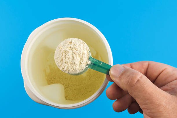 istock Male hand holds full measuring spoon with protein powder, directly above an almost empty container on blue background, sports nutrition 670150586