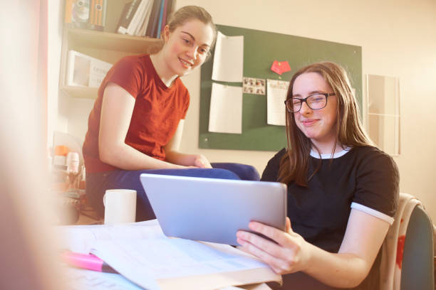 istock Two students smiling  as they look at digital tablet in dorm room 670168200