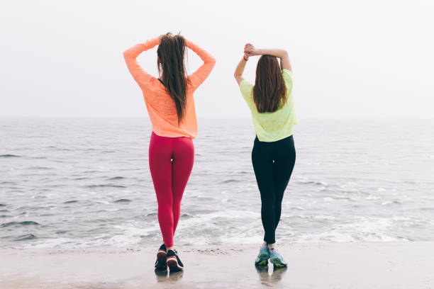 Two beautiful slender young girls are engaged in gymnastics on the beach Two beautiful slender young girls are engaged in gymnastics on the beach, view from the back backside for a girl on the beach stock pictures, royalty-free photos & images