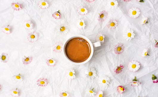 Cup of coffee and daisy flowers on white fabric