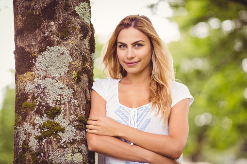 Smiling woman with arms crossed standing by tree in park