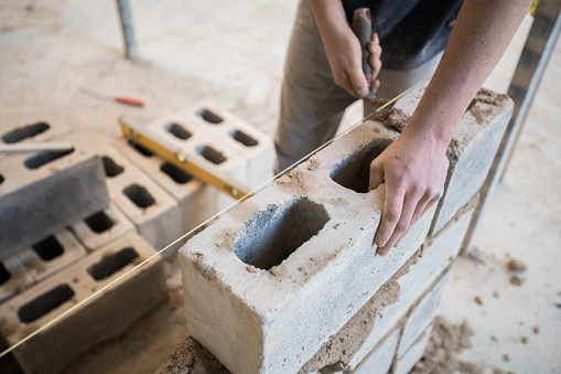 Hand of a mason laying a hollow concrete cinder block.