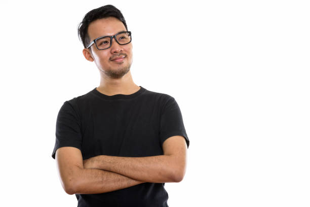 Studio shot of young Asian man thinking while wearing eyeglasses with arms crossed horizontal shot