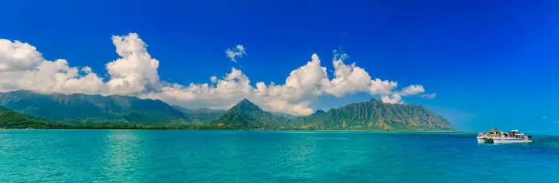 Photo of Panoramia of tropical lagoon, lush mountains, a catamaran and the ocean in Oahu, Hawaii