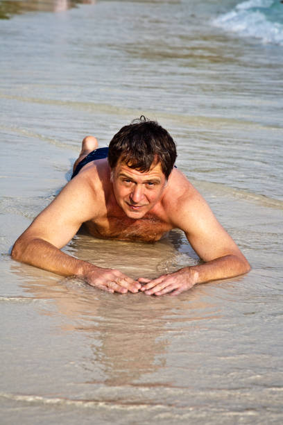 istock Man in bathingsuit is lying at the beach and enjoying the saltwater with tiny waves 670273668