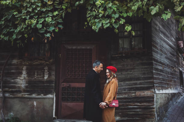 european couple at street, autumn look, casual style. red beret and coat. wooden facade of old building - sexual issues sexual activity couple tan imagens e fotografias de stock