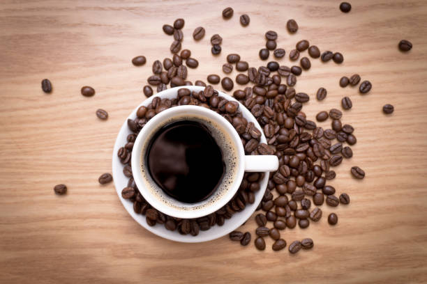 istock White cup with black, hot coffee standing on brown, roasted beans on wood table. 670310424