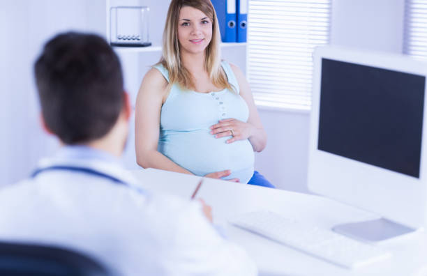 istock Smiling pregnant patient looking at camera while doctor taking notes 670312614