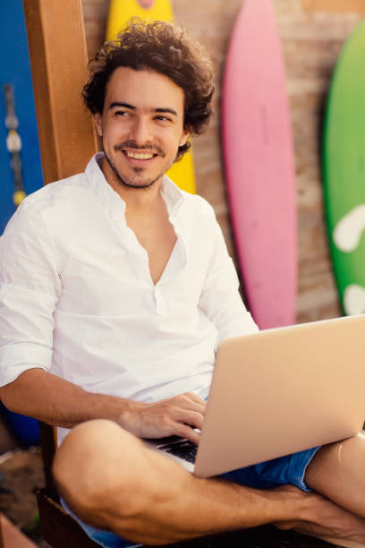 istock Attractive man using a laptop at a beach bar 670313104