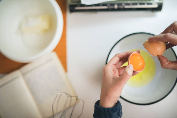 mani femminili che tengono l'uovo incrinato sopra una ciotola bianca - eggs animal egg cracked egg yolk foto e immagini stock