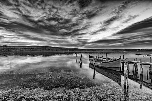 exciting black and white landscape on a lake with wooden pier and boat .