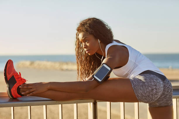 спортивная женщина растяжения ноги на перила на пляже - railing beautiful human leg people стоковые фото и изображения