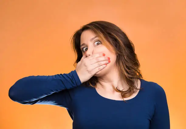 Closeup portrait middle aged business woman, worker, scared employee, covering mouth. Speak no evil concept, isolated orange background. Human emotions, face expression, feeling, sign, body language