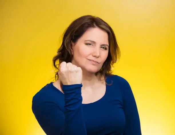 Closeup portrait angry cranky upset middle aged woman worker, business employee showing fist, warning someone, stay away isolated yellow background. Negative emotion, facial expression feeling reaction