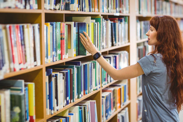 istock Mature student picking book in library wearing smart watch 670367800