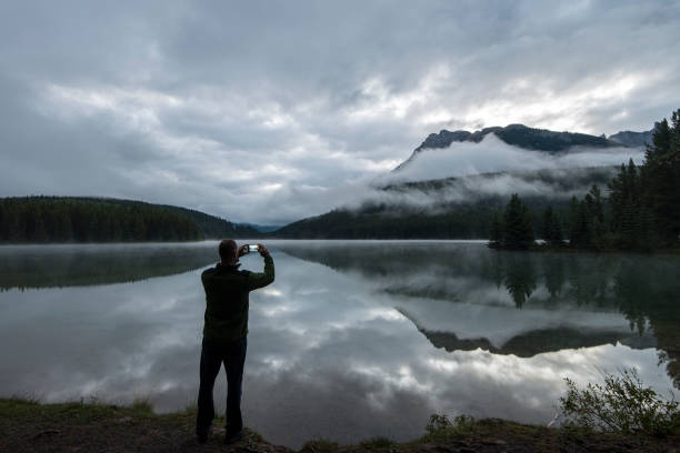 istock Man takes smart phone pic at mtn lake, am 670383253