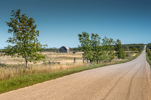 Very straight long road in rural area with hay field and barn and trees.  Road leads into
