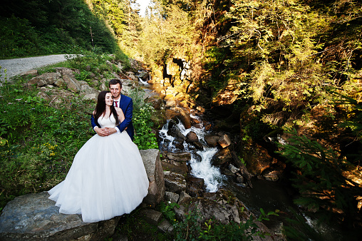 Lovely wedding couple against river with stones at Carpathian mountains.