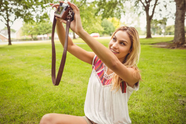 istock Smiling woman taking self portrait with camera while sitting on grass 670393770