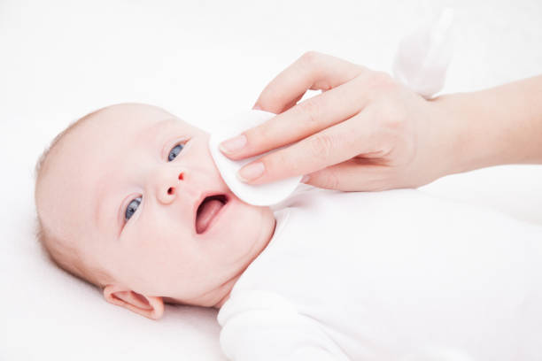 mother cleans face of a newborn baby whith a cotton pad stock photo
