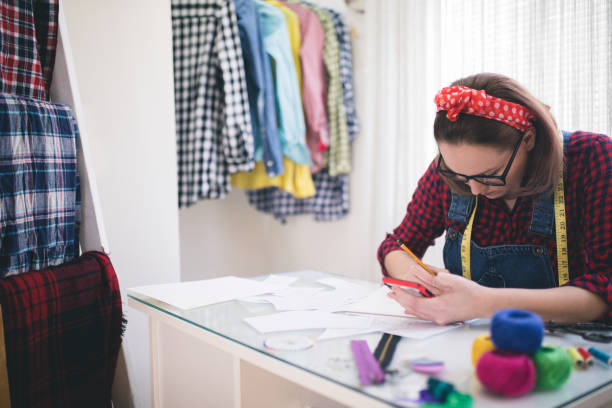 istock Young fashion designer talking on cellphone, watching her designs 670402748