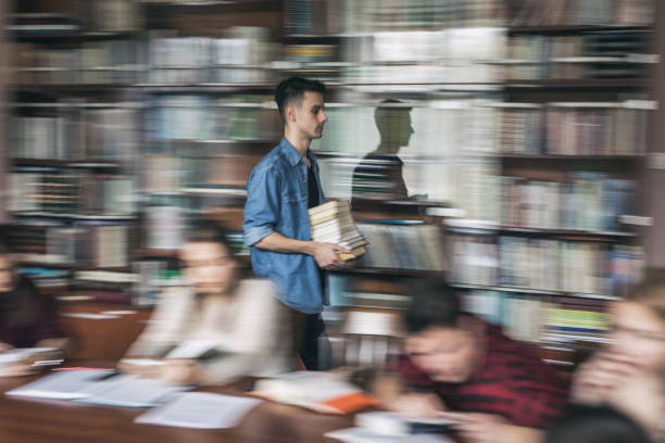 istock Male student in blurred motion carrying stack of books in library. 670407812