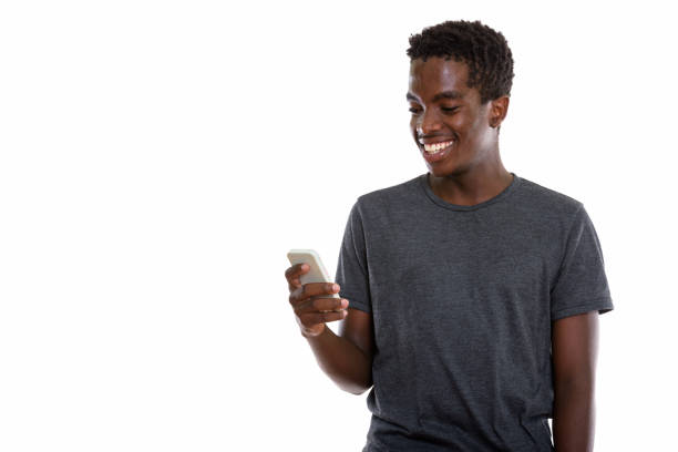 tiro de estúdio de jovem feliz preto africano adolescente sorrindo enquanto estiver usando o celular - text messaging mobile phone teenagers only people - fotografias e filmes do acervo