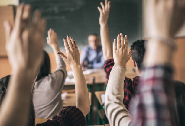 We all know the answer! Rear view of group of students raising hands to answer teacher's question in the classroom. Focus is on hands in the middle. arms raised stock pictures, royalty-free photos & images