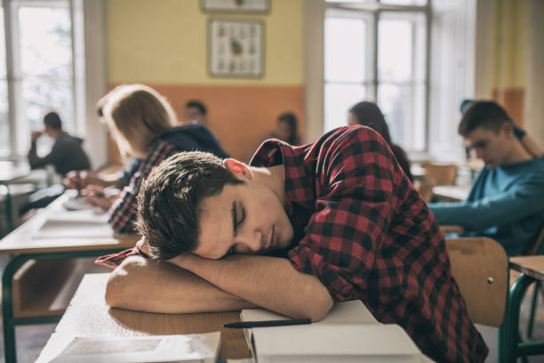 Student falling asleep during lecture. Male student in high school uniform in school math class.