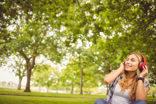 Happy woman enjoying music with eyes closed while sitting on grass at park