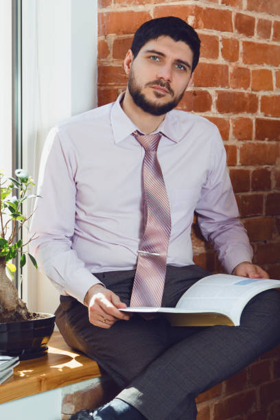 istock A young man reading a magazine at the window in the office. 670438192