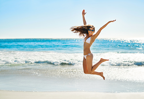 Shot of a young woman jumping into mid air on the beach