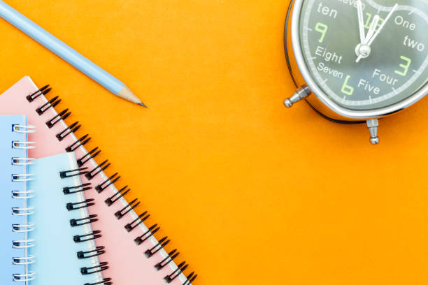 istock pencil with notebook and alarm clock on orange paper background. 670467098
