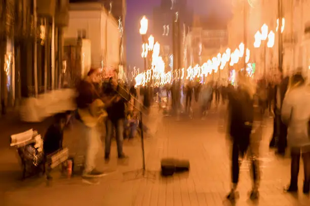 Abstract vintage tone motion, blurred image of street musicians, spectators and bright city lights with bokeh, night urban street life, motion blur concept, for background use