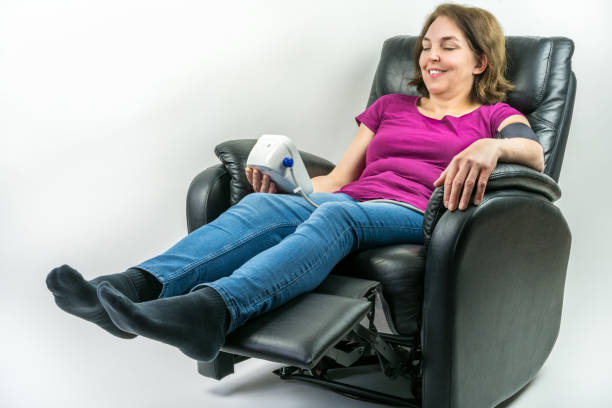 Pretty middle-age woman resting in black leather recliner armchair. Checking blood pressure using portable blood pressure machine. stock photo