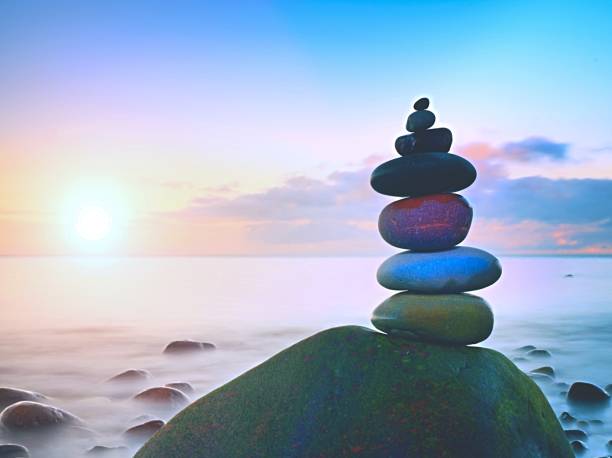 istock Stacked rounded stones at sea. Small polished pebbles stack on dark wet rock,  blue smooth water of ocean in background 670481360