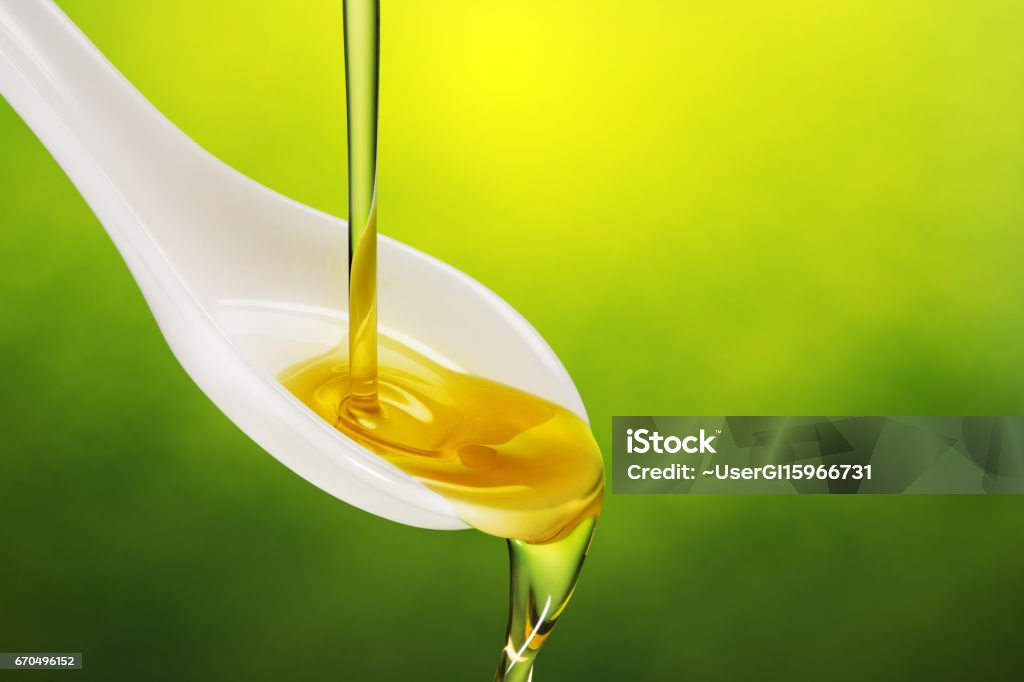 extra virgin olive oil poured in a spoon extra virgin olive oil poured in a spoon overflowing on green background Olive Oil Stock Photo