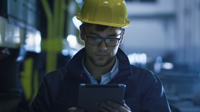 Technician in Glasses and Hard Hat Using Tablet in Industrial Environment