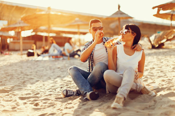 istock Happy young couple drinking beer and having fun at the beach during sunset 670510910