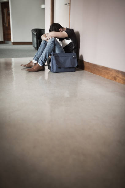 istock Male student with head on knees sitting by wall 670517094