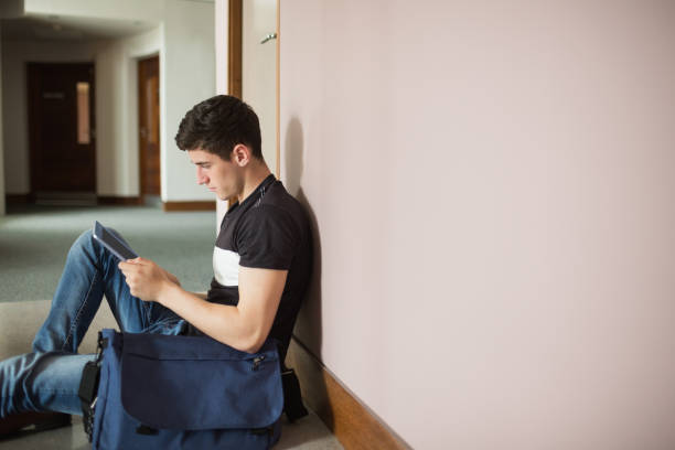 istock Male student with digital tablet sitting by wall 670517556