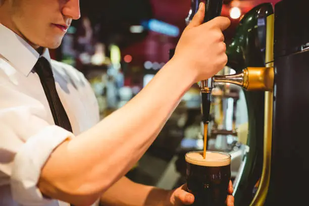 Cropped image of bartender holding beer glass below dispenser tap at bar counter