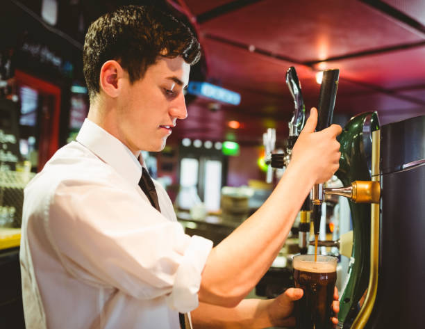 istock Barkeeper holding beer glass below dispenser tap 670537002