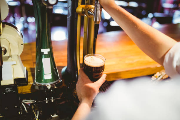 istock Barkeeper holding glass below beer dispenser tap 670537026
